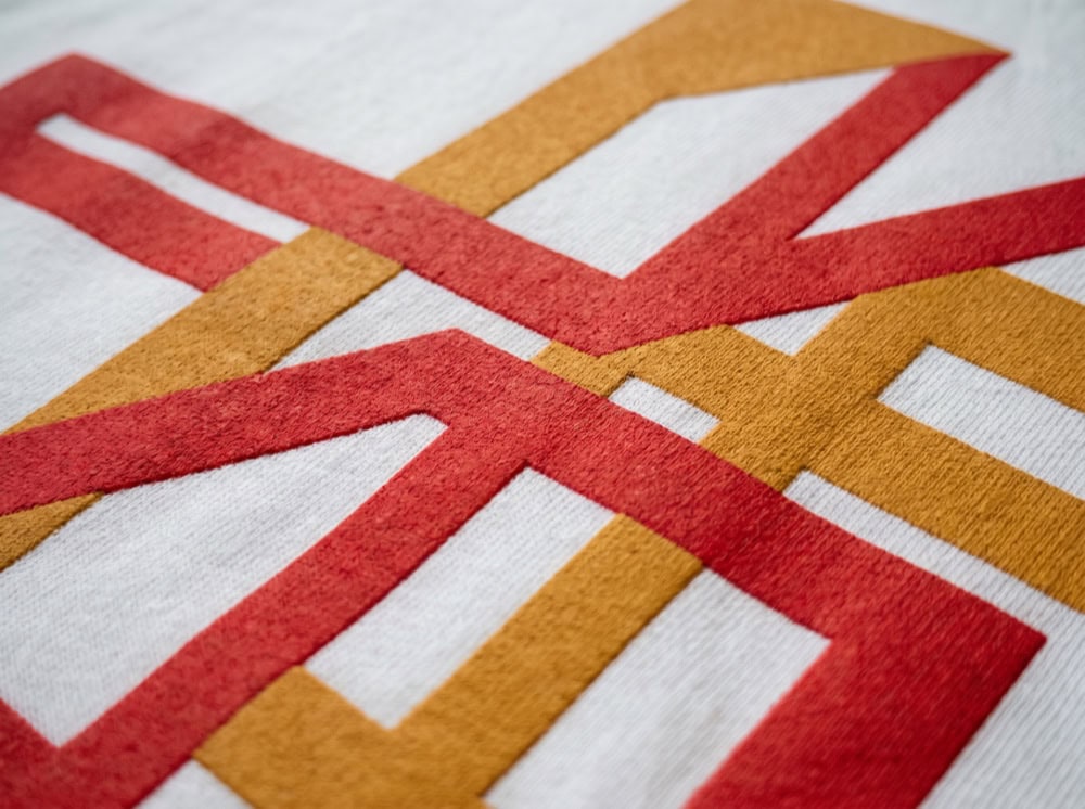 Primer plano de una tela blanca con líneas geométricas rojas y naranjas superpuestas que forman figuras abstractas, ideal para la personalización textil.
